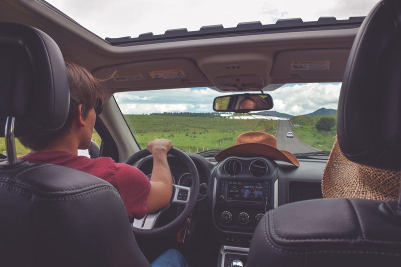 photo of two people driving in the countryside with a cowboy hat on the dashboard